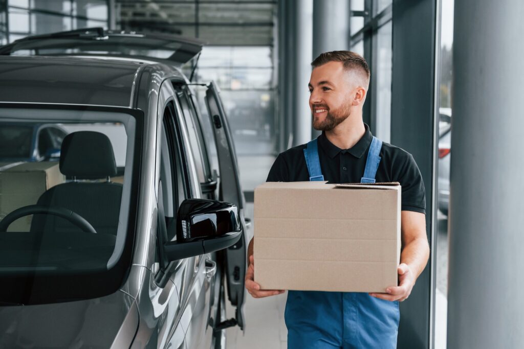 Paper box. Delivery man in uniform is indoors with car and with order